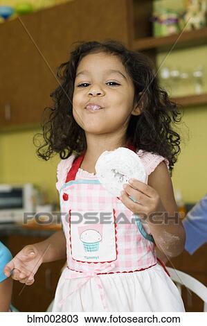 Stock Image - Hispanic girl eating powdered doughnut. Fotosearch