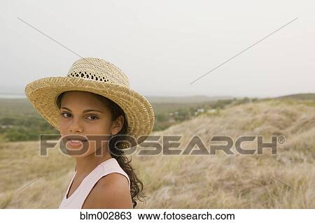 Stock Image - Hispanic girl in straw hat in remote field. Fotosearch