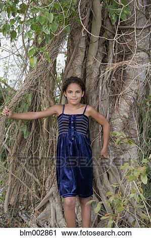 Stock Image - Hispanic girl leaning against mass of tree roots. Fotosearch