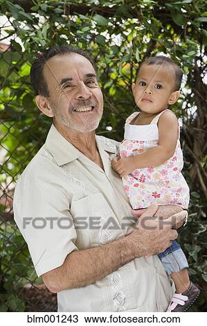 Stock Image - Hispanic grandfather holding granddaughter. Fotosearch