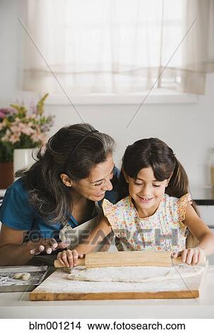 Picture - Hispanic grandmother and granddaughter rolling dough. Fotosearch