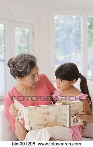 Stock Photo - Hispanic grandmother and granddaughter looking at scrapbook. Fotosearch