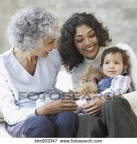 Stock Photo - Hispanic grandmother, mother and baby smiling on sofa. Fotosearch