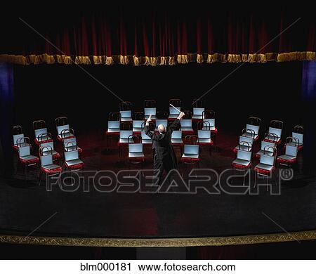 Stock Image - Hispanic male conductor in front of laptops on chairs . Fotosearch