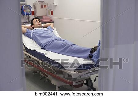 Stock Image - Hispanic male doctor laying in hospital bed. Fotosearch