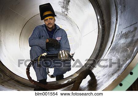 Picture - Hispanic male welder inside large metal pipe. Fotosearch