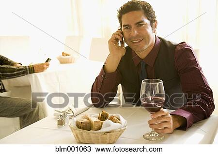 Hispanic man drinking wine and talking on cell phone in restaurant View Large Photo Image Stock Image - Hispanic man drinking wine and talking on cell phone in restaurant. Fotosearch
