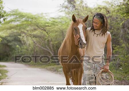 Stock Photography - Hispanic man leading horse down dirt road. Fotosearch
