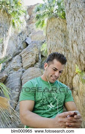 Stock Photography - Hispanic man listening to mp3 player in tropical area. Fotosearch