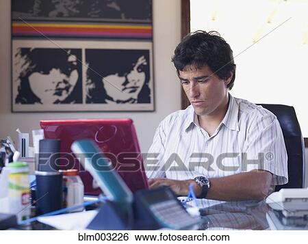 Hispanic man sitting a desk using laptop View Large Photo Image Stock Photograph - Hispanic man sitting a desk using laptop. Fotosearch