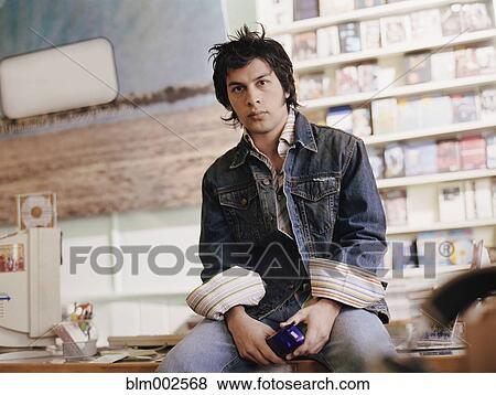 Stock Photo - Hispanic man sitting on music store counter. Fotosearch