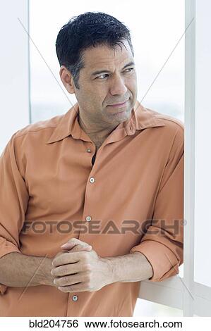 Stock Photograph - Hispanic man standing in window. Fotosearch