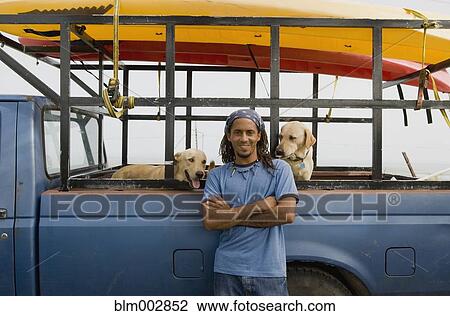 Stock Image - Hispanic man with dogs leaning against truck. Fotosearch