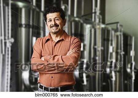 Stock Photography - Hispanic manager standing near vats in factory. Fotosearch