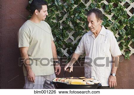 Stock Photograph - Hispanic men barbecuing on patio. Fotosearch