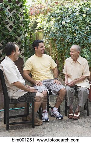 Stock Image - Hispanic men sitting on patio. Fotosearch