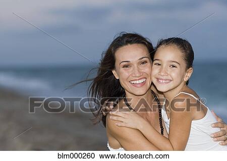 Stock Image - Hispanic mother and daughter hugging on beach. Fotosearch