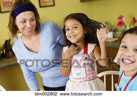 Stock Image - Hispanic mother and daughters in kitchen. Fotosearch