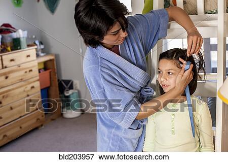 Stock Photo - Hispanic mother brushing daughter's hair. Fotosearch