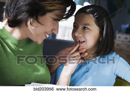 Stock Photograph - Hispanic mother examining daughter's missing tooth. Fotosearch