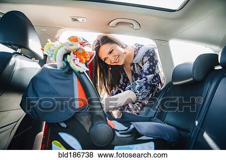 Stock Photo - Hispanic mother fastening car seat in car. Fotosearch