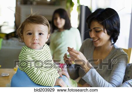 Stock Photo - Hispanic mother feeding toddler in kitchen. Fotosearch