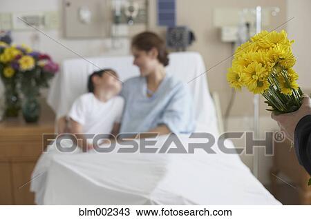 Stock Image - Hispanic mother in hospital bed hugging son. Fotosearch