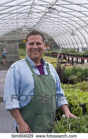 Stock Photo - Hispanic nursery worker standing by plants. Fotosearch