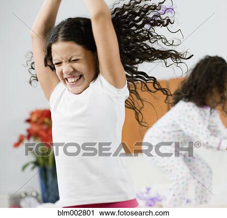 Stock Image - Hispanic sisters jumping on bed. Fotosearch