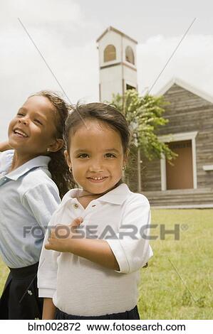 Stock Image - Hispanic sisters standing outside church. Fotosearch