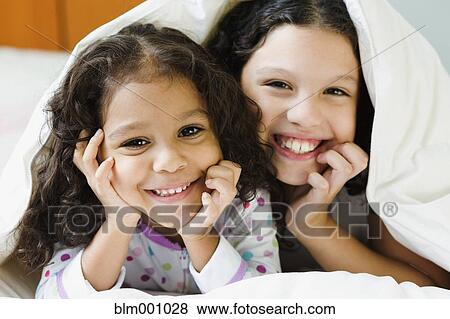 Stock Photo - Hispanic sisters underneath blanket. Fotosearch