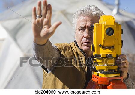 Stock Image - Hispanic surveyor working outdoors. Fotosearch