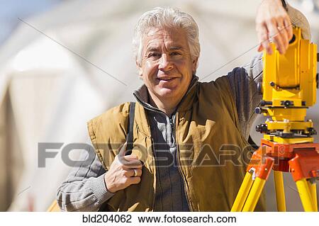 Stock Image - Hispanic surveyor working outdoors. Fotosearch