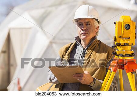 Stock Image - Hispanic surveyor working outdoors. Fotosearch