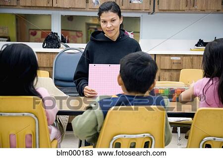 Stock Image - Hispanic teacher sitting at table with students. Fotosearch