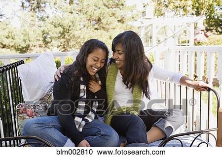 Stock Image - Hispanic teenager and woman laughing on porch. Fotosearch