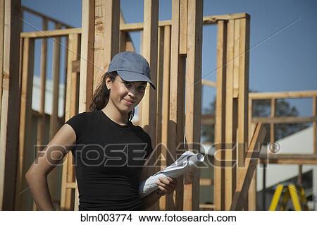 Picture - Hispanic woman holding blueprints at construction site. Fotosearch