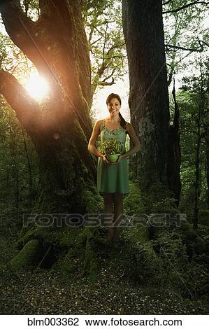 Stock Image - Hispanic woman holding potted plant in forest. Fotosearch
