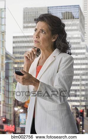 Stock Photograph - Hispanic woman in city holding cell phone and looking confused. Fotosearch