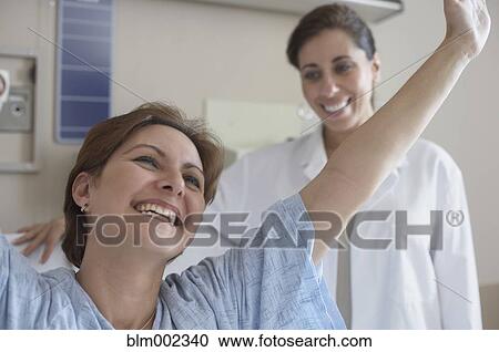 Stock Image - Hispanic woman in hospital gown with arms raised. Fotosearch