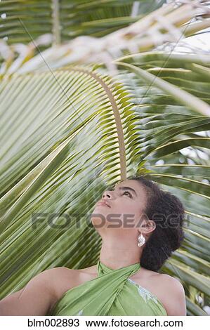 Stock Image - Hispanic woman in sarong near palm leaf. Fotosearch