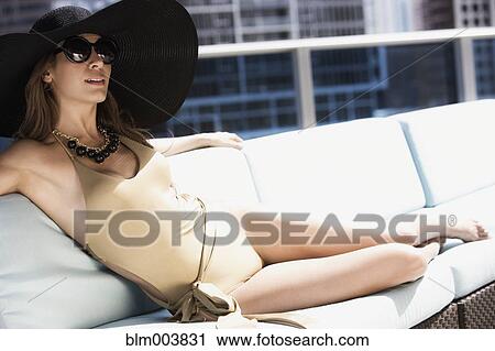 Stock Image - Hispanic woman on lounge chair wearing bathing suit and sun hat. Fotosearch