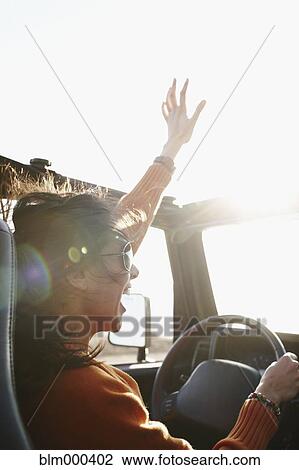 Stock Image - Hispanic woman raising arms while driving. Fotosearch