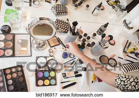 Stock Photo - Hispanic woman selecting makeup from table. Fotosearch
