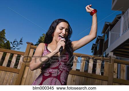 Stock Photography - Hispanic woman singing karaoke in backyard. Fotosearch