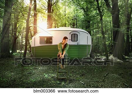 Stock Photograph - Hispanic woman sitting by camper in forest. Fotosearch
