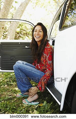 Stock Image - Hispanic woman sitting on side of car. Fotosearch