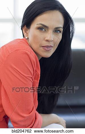Stock Image - Hispanic woman smiling on sofa. Fotosearch