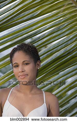 Picture - Hispanic woman standing near palm leaf. Fotosearch