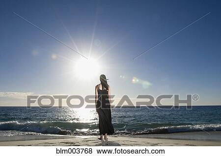 Stock Photo - Hispanic woman standing on beach at waterÆs edge. Fotosearch